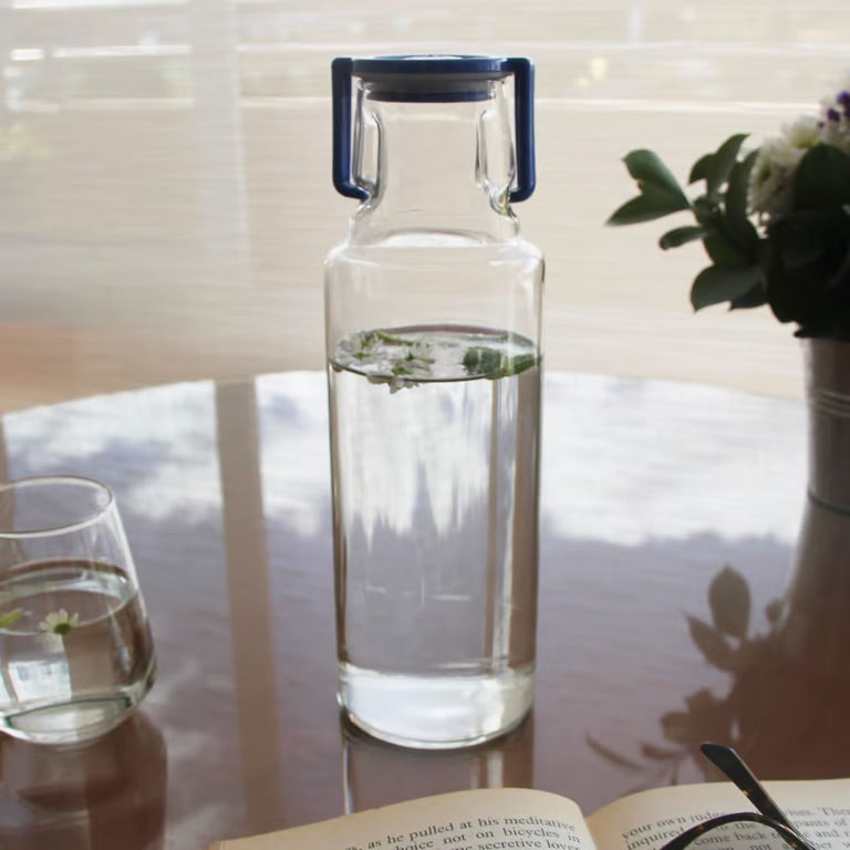 botella fenicie de vidrio en mesa con libro y tapa azul ambientada