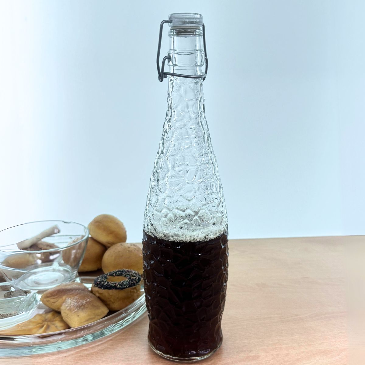 botella de vidrio con jugo en mesa de madera y con pastelillos en un lado