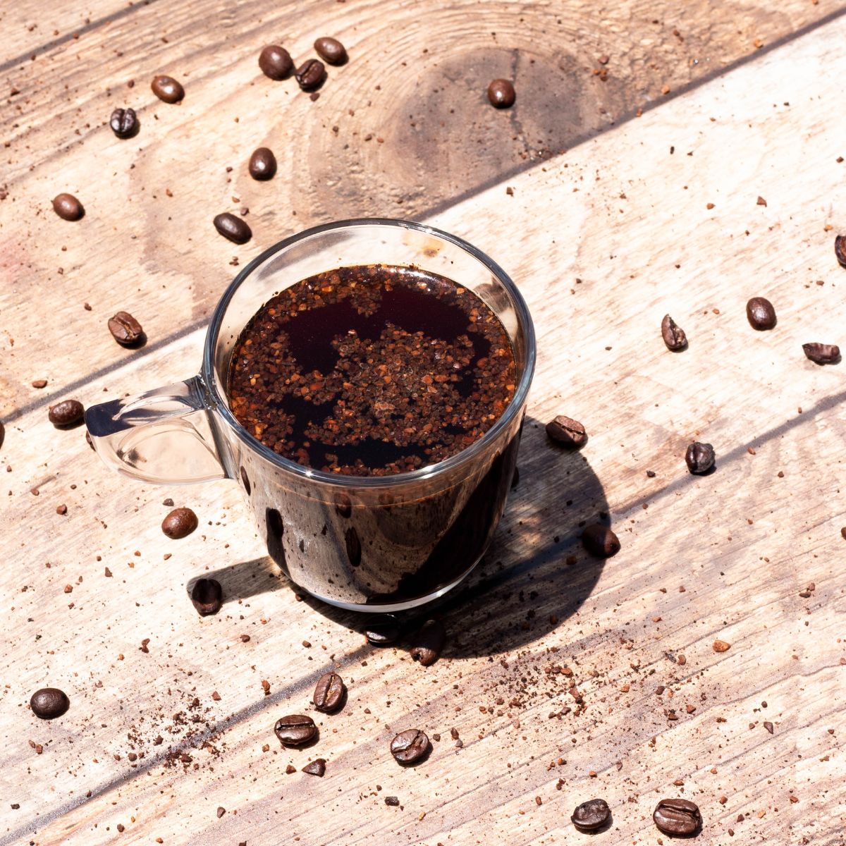Vista superior de taza de vidrio Alpi con café molido y granos, diseño robusto y transparente.