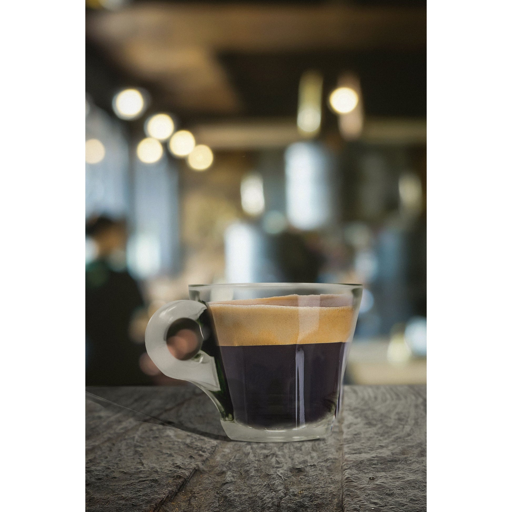 Taza Conic de vidrio con café negro servida sobre mesa de cafetería, diseño moderno y resistente al calor.