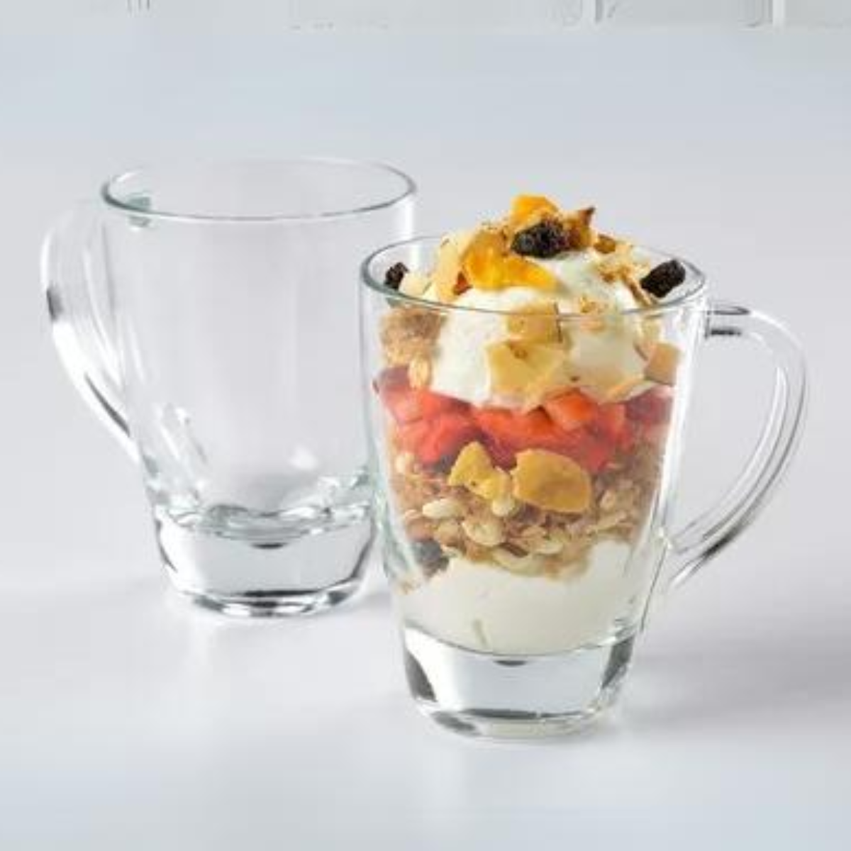 Tazas de vidrio Pergamino usadas para servir postre con yogur, granola y frutas frescas.