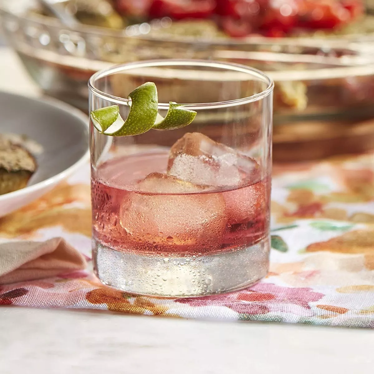 Vaso Stelvio rocks de vidrio con cóctel rosa y hielo sobre mesa